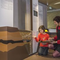 Deux visiteurs, une mère et sa fille, dans le parcours d'exposition du CIP La Villa, musée d'archéologie à Dehlingen. On peut y voir une coupe de terrain permettant de montrer comment les archéologues déterminent l'âge de vestiges anciens